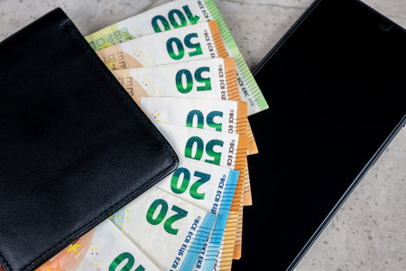 Paper money in black partmone and smartphone on the table. Cash euro bills in leather wallet with...