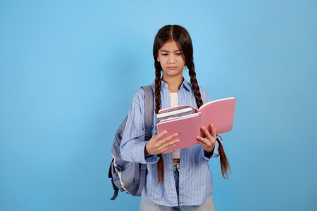 Teenage girl books and notebooks with bag and looks dissatisfied on blue background.の写真素材