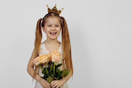 Little smiling girl holding flowers and wearing crown. International women's day.の写真素材