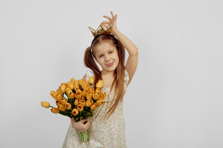 Little smiling girl holding flowers and wearing crown. International women's day.の写真素材
