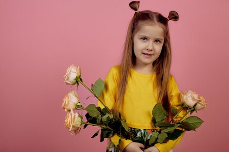 Little smiling girl holding flowers on pink background. International women's day.の写真素材