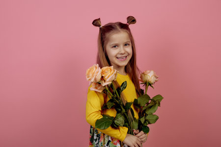 Little smiling girl holding flowers on pink background. International women's day.の写真素材