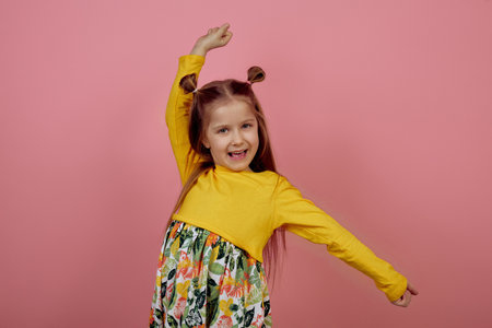 Little smiling girl with hands up on pink backgroundの写真素材