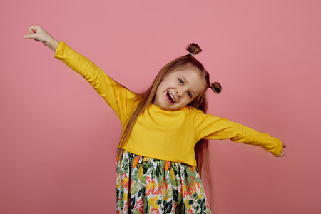 Little smiling girl with hands up on pink backgroundの写真素材