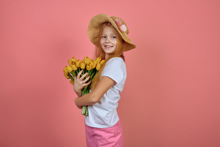 Teen redhead smiling girl with yellow tulips, flowers on pink background with hat. International women's day.の写真素材