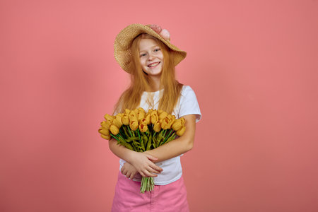 Teen redhead smiling girl with yellow tulips, flowers on pink background with hat. International women's day.の写真素材
