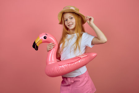 Redhead teen girl with flamingo pool float toy wearing hat on pink background. Summer, vacationの写真素材