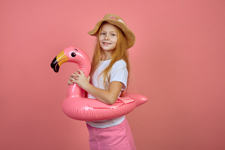 Redhead teen girl with flamingo pool float toy wearing hat on pink background. Summer, vacationの写真素材