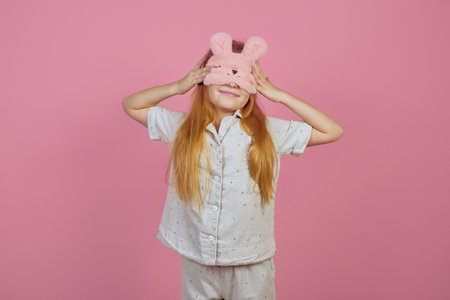 Smiling redhead teen girl wearing sleeping mask on pink background.の写真素材