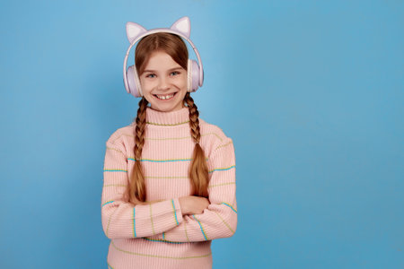 Little smiling girl with headphones on her head on blue background.の写真素材