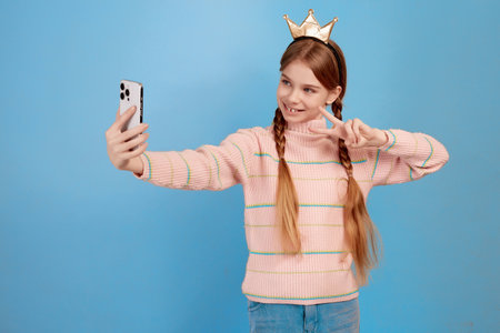 Little girl with crown have video call with her phone and showing peace symbol with hand.の写真素材