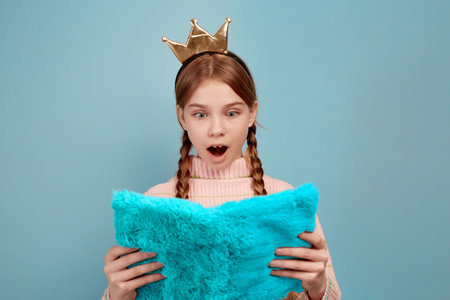 Little surprised girl with golden crown holding notebook on blue background.の写真素材