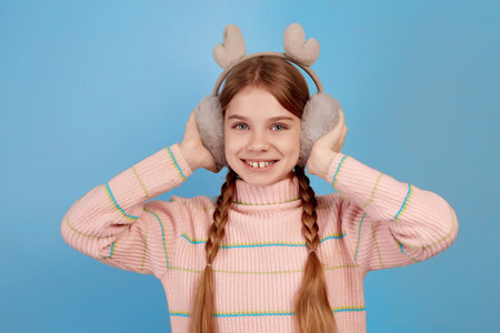 Little smiling girl wearing fluffy headphones on blue background. Close portrait.の写真素材