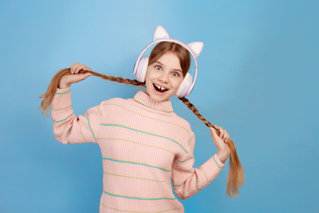 Little smiling girl with headphones on her head holding pigtails on blue background.の写真素材