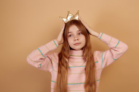 Little cute girl holding golden crown by hands on beige background.の写真素材