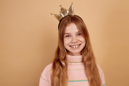 Little smiling girl with golden crown on beige background.の写真素材