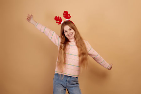 Smiling girl in decorative deer horns dancing on beige background.の写真素材