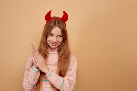 Little tricky girl with red devil horns on beige background.の写真素材