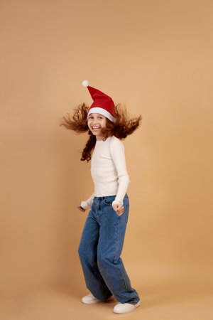 Little smiling Afro-American girl with Santa hat jumps on beige background.の写真素材
