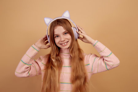 Smiling little girl in headphones with ears on beige backgroundの写真素材