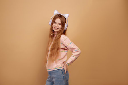 Smiling little girl in headphones with ears on beige backgroundの写真素材