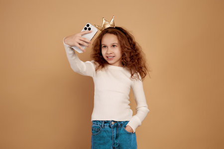 Little African-American girl with long curly hair holding phone and takes selfie on beige background.の写真素材