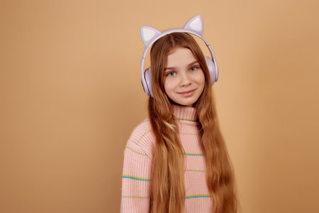 Smiling little girl in headphones with ears on beige backgroundの写真素材
