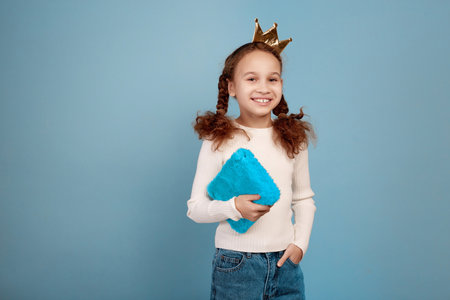 Happy little African-American girl with crown and notebook in hands on blue background.の写真素材