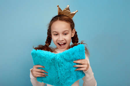 Happy little African-American girl with crown and notebook in hands on blue background.の写真素材