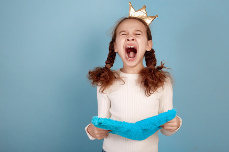 Angry little African-American girl with crown and notebook in hands on blue background.の写真素材