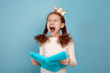 Tired little African-American girl with crown and notebook in hands on blue background.の写真素材