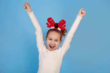 Happy little African-American girl with decorative deer horns with hands up on blue background.の写真素材