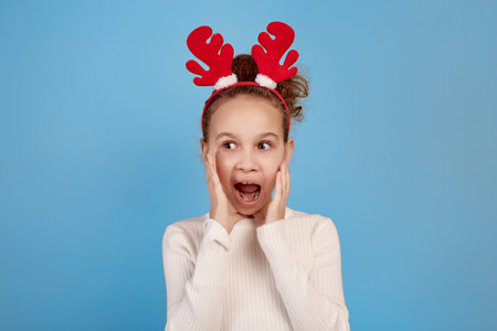 Surprised little African-American girl with decorative deer horns with hands near face on blue background.の写真素材