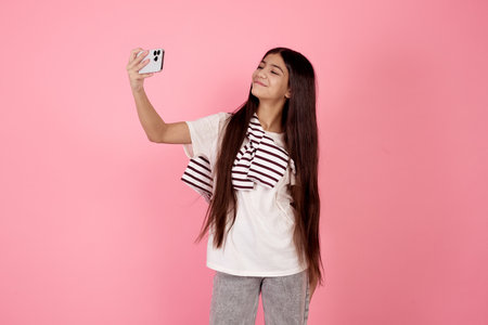 Young smiling teenage girl taking a selfie with phone on pink background in studio.の写真素材