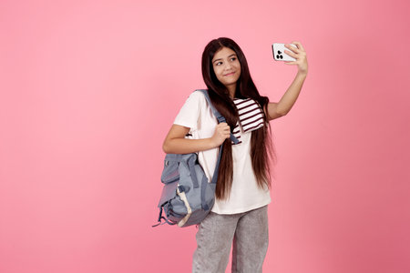 Young smiling teenage girl taking a selfie with phone with bag on pink background in studio.の写真素材