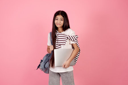 Young smiling teenage girl with bag and laptop on pink background in studio.の写真素材