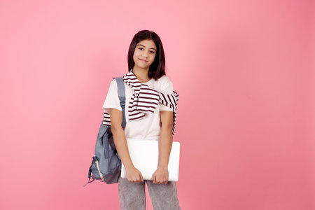 Young smiling teenage girl with bag and laptop on pink background in studio.の写真素材