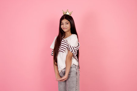Young smiling and shy teenage girl with crown on pink background in studio.の写真素材