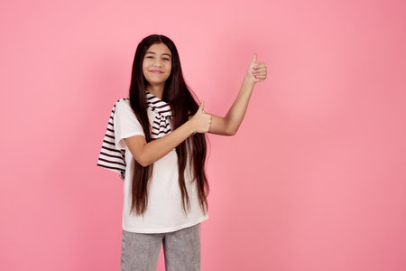 Young smiling teenage girl and laptop shows aside by hands on pink background in studio.の写真素材
