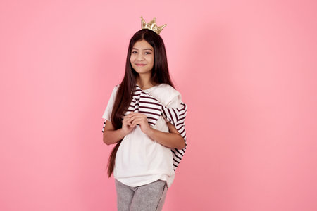 Young smiling and shy teenage girl with crown on pink background in studio.の写真素材