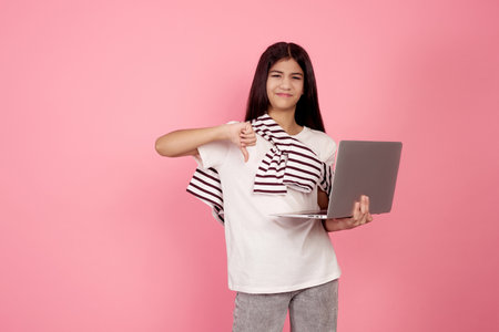 Young upset teenage girl and laptop shows thumb down on pink background in studio.の写真素材
