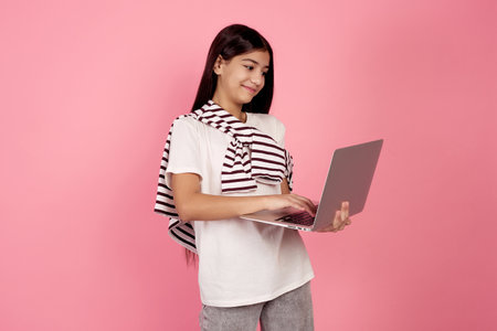 Young smiling teenage girl and laptop on pink background in studio.の写真素材