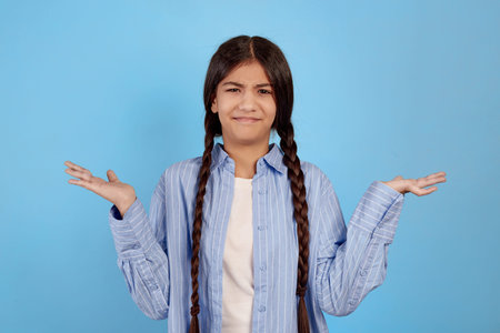 Teenage girl looks malcontent and dissatisfied on blue background.の写真素材