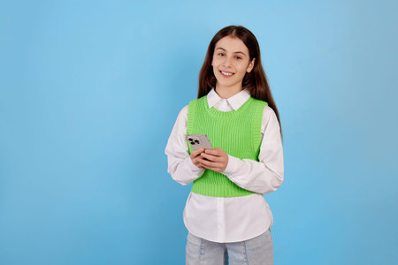 Young brunette teenage girl with phone on blue background.