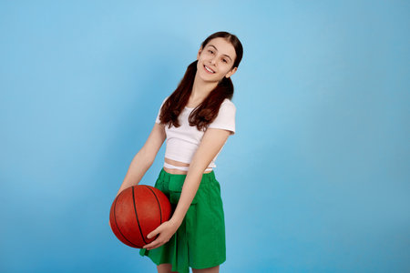 Young brunette teenage girl with basket ball and ponytails on blue background.の写真素材