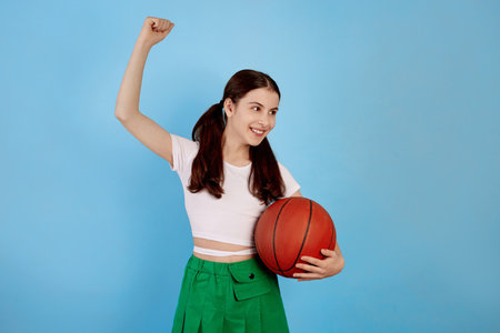Young brunette teenage girl with basket ball and ponytails on blue background.の写真素材