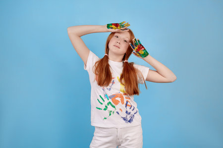 Happy and cheerful ginger teenage girl showing painted hands on blue background in studio.の写真素材