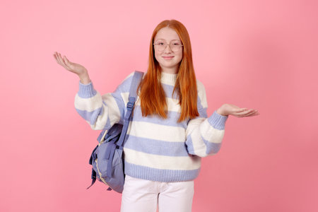 Smiling redhead teenage girl with bag wearing glasses on pink background in studio.の写真素材