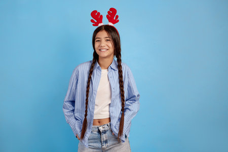 Smiling teenage girl with decorative deer horns and pigtails on blue background.の写真素材