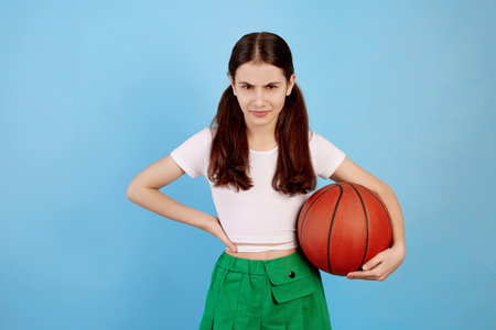 Young brunette teenage girl with basket ball and ponytails on blue background.の写真素材